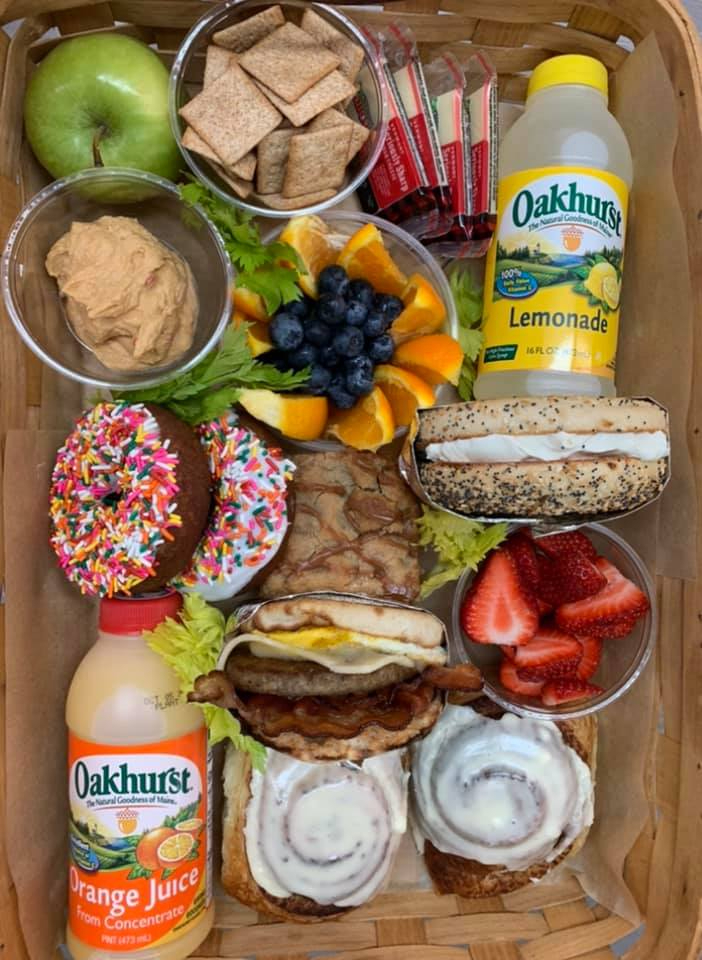 a basket of breakfast sandwiches, bagels, fruit, donuts, drinks and more.